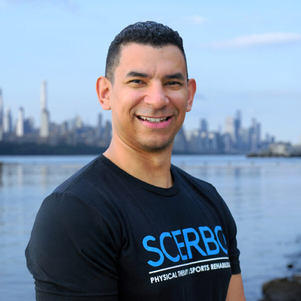 Dr. Frankie Goris of Scerbo Physical Therapy standing along the Hudson River Waterfront Walkway with the New York City skyline in the background.