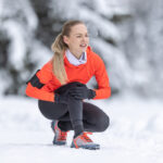 A young woman runner holds her knee after straining pain on her cruciate ligament during a cross-country training in the snow during the winter season