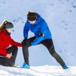 Man running in the snow with his wife holds his knee do to joint pain.