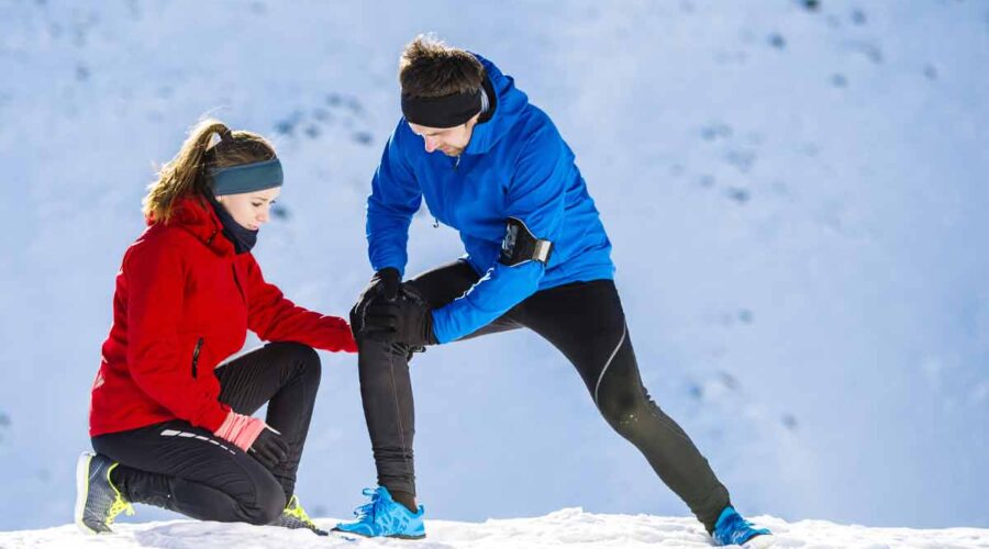 Man running in the snow with his wife holds his knee do to joint pain.