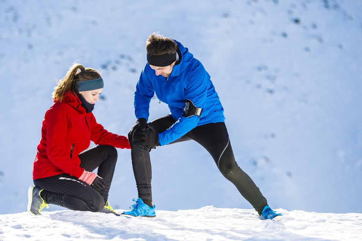 Man running in the snow with his wife holds his knee do to joint pain.