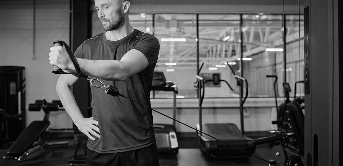 Man doing cable machine lateral raises extension exercises at a gym.