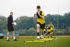 A young soccer player doing sport training drills under the supervision of his sports coach 