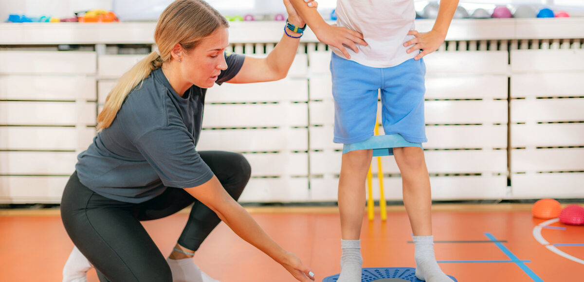 A young boy exercising with balancing discs and resistance bands under the care of female physical therapist