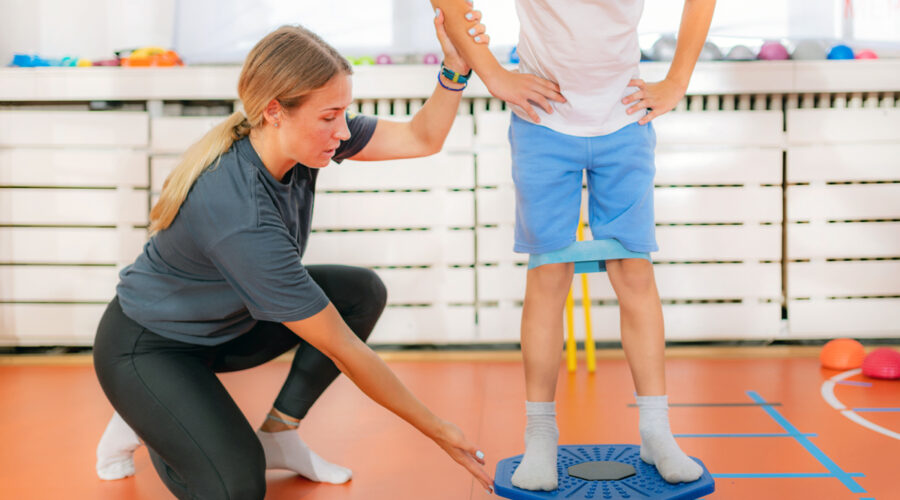 A young boy exercising with balancing discs and resistance bands under the care of female physical therapist