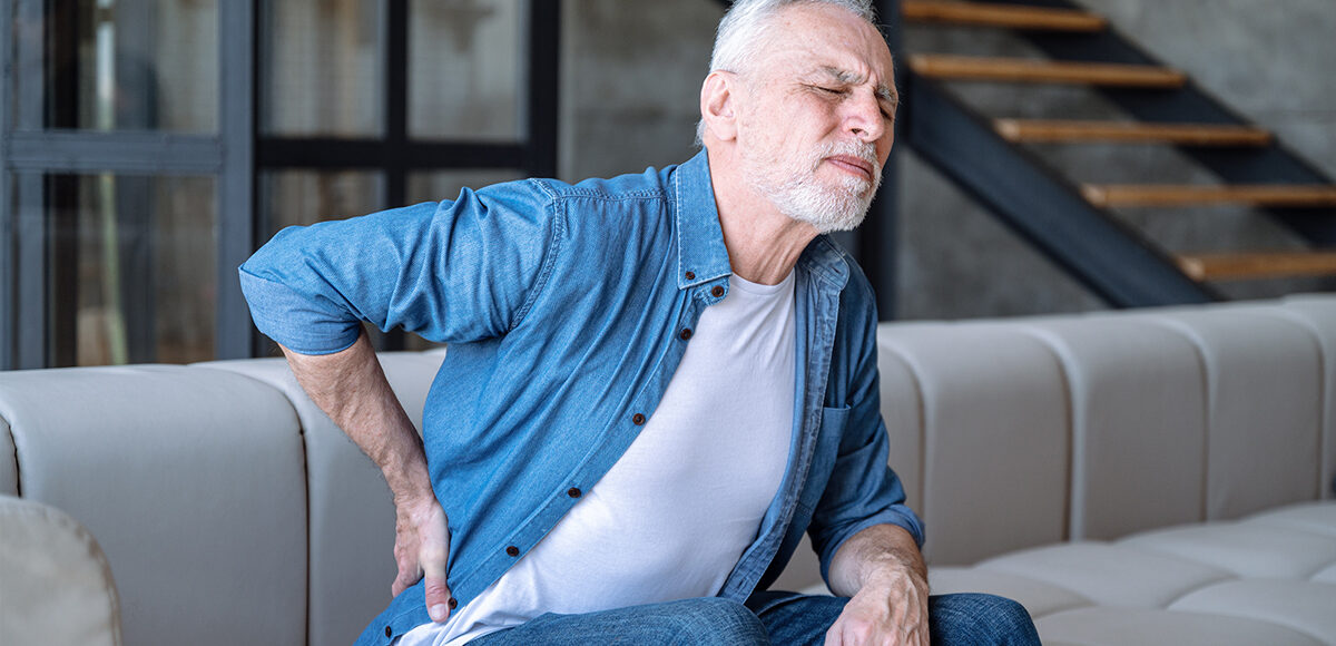 Elder man holding his hip in pain while sitting in his home sofa