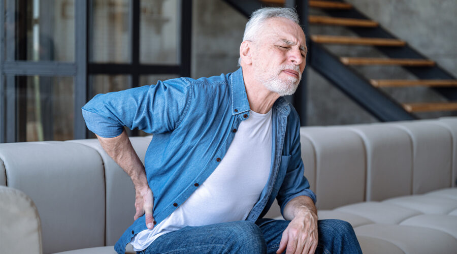 Elder man holding his hip in pain while sitting in his home sofa