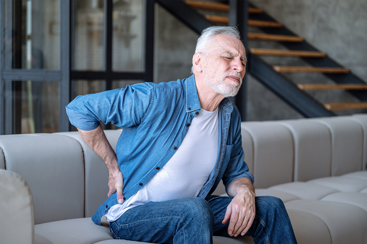 Elder man holding his hip in pain while sitting in his home sofa