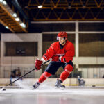 A hockey player in red uniform skating to goal with stick and puck.
