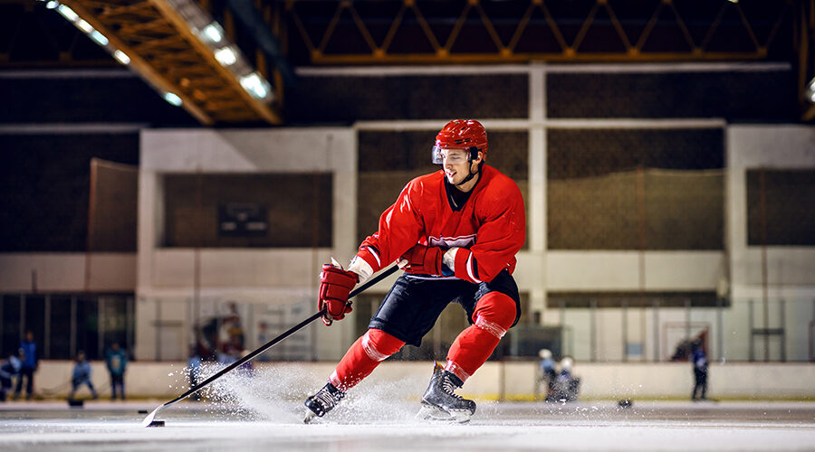 A hockey player in red uniform skating to goal with stick and puck.