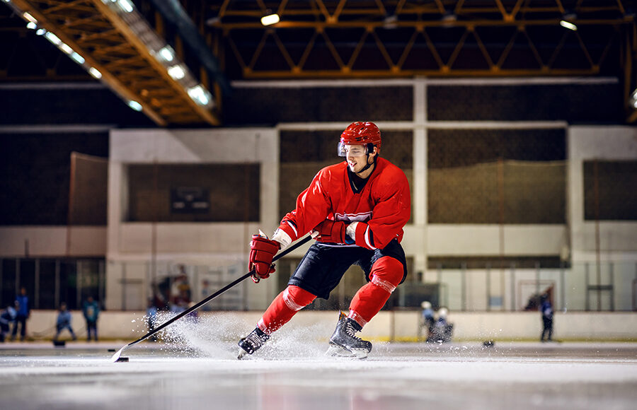 A hockey player in red uniform skating to goal with stick and puck.