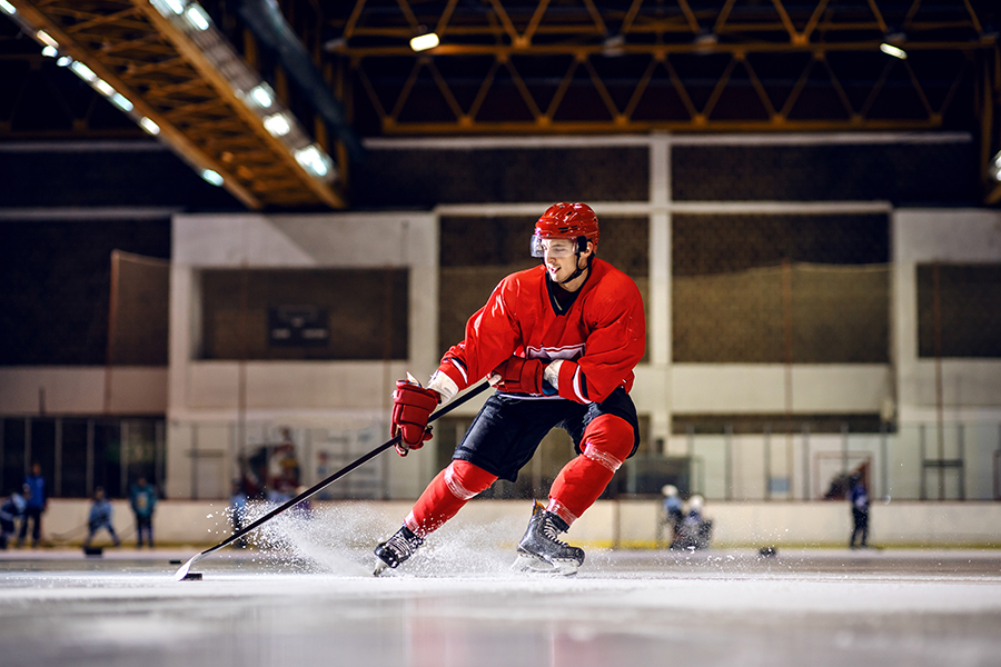 A hockey player in red uniform skating to goal with stick and puck.