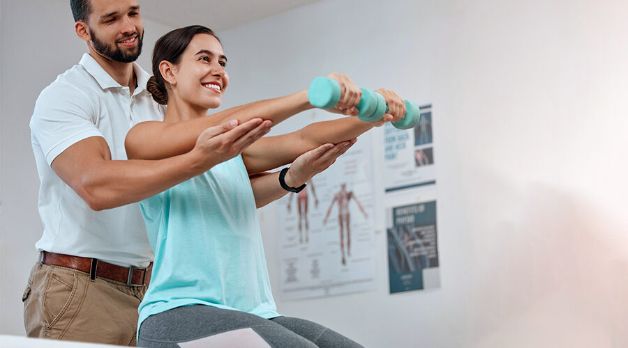 Young woman sitting on a exercise table doing dumbbells with the help of male physical therapist