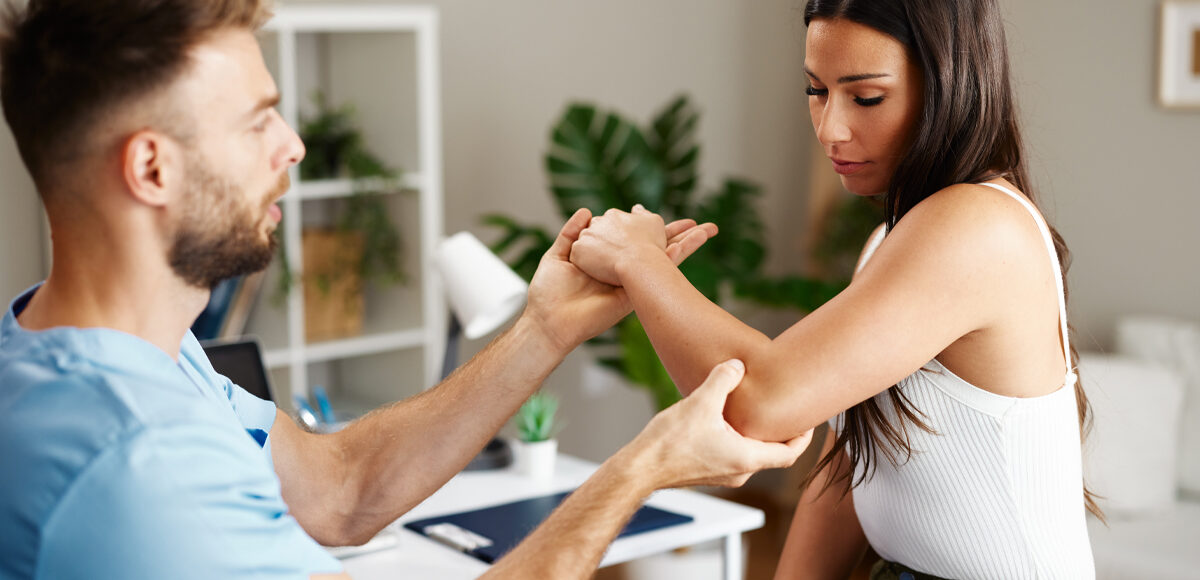 Male physical therapist asses elbow of female patient during a physical evaluation