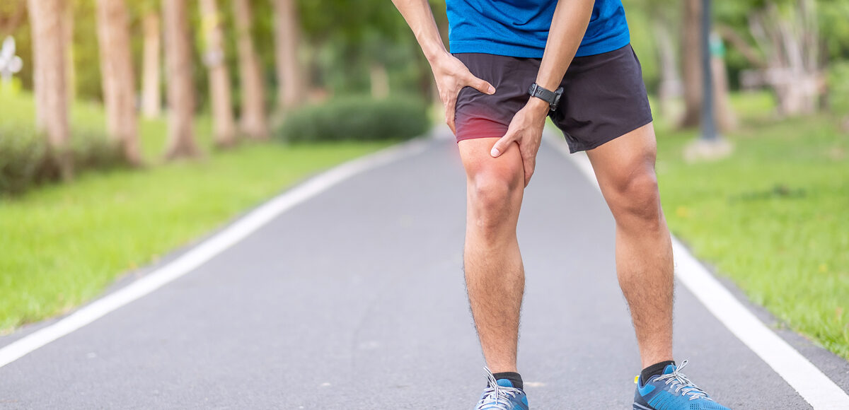 A young adult male stops and holds his knee do to muscle pain while running.