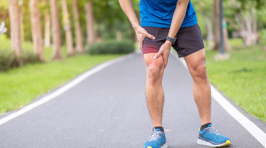 A young adult male stops and holds his knee do to muscle pain while running.