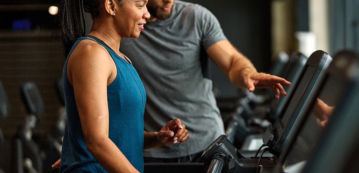 Male physical therapist showing female patient how to setup a treadmill level.