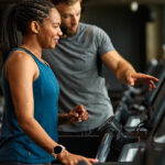 Male physical therapist showing female patient how to setup a treadmill level.