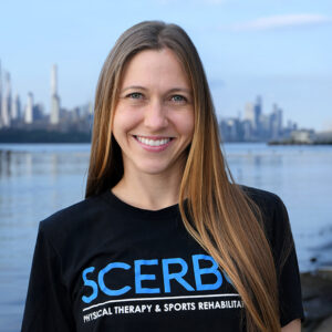 Kelly Wieczerzak of Scerbo Physical Therapy standing on the Hudson River Waterfront Walkway with the New York City skyline in the background.