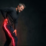 Middle-aged man holding his lower back and hip in pain, with a red and yellow electric spark extending from his hip down his leg to represent nerve pain.