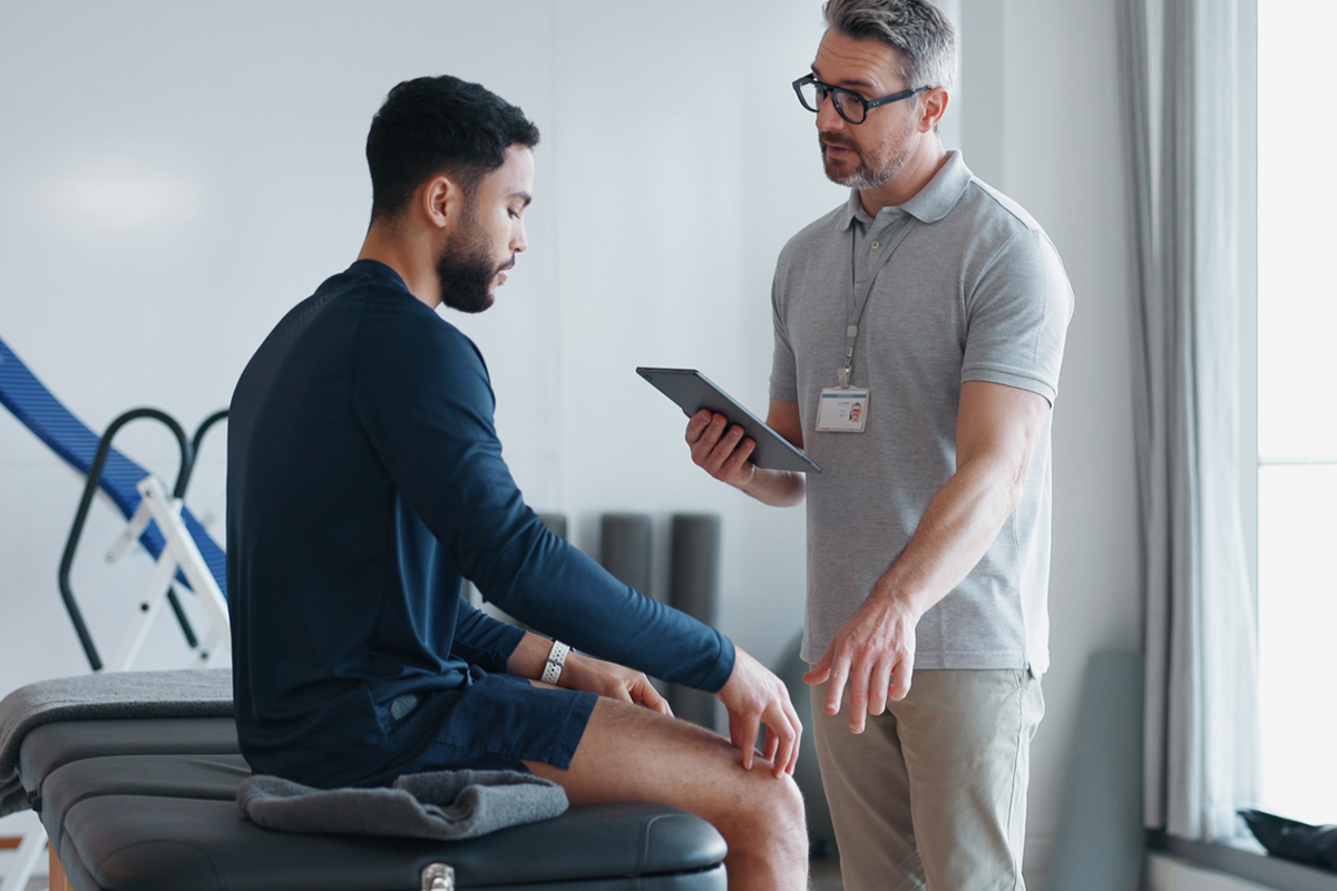 Male physical therapist conducting a physical assessment of a young male patient to evaluate mobility, strength, and range of motion.